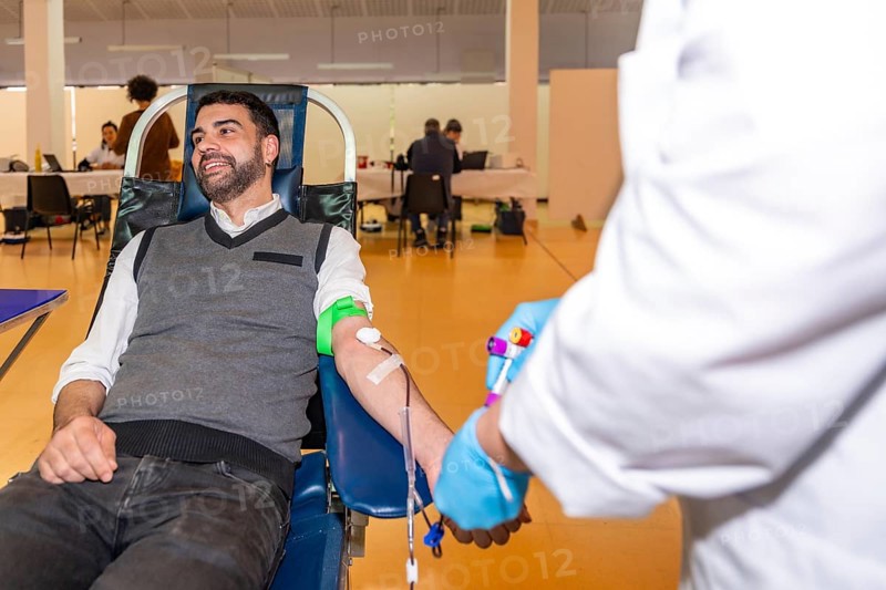 Man sitting on a comfortable chair while donating blood in a center next to a nurse in uniform