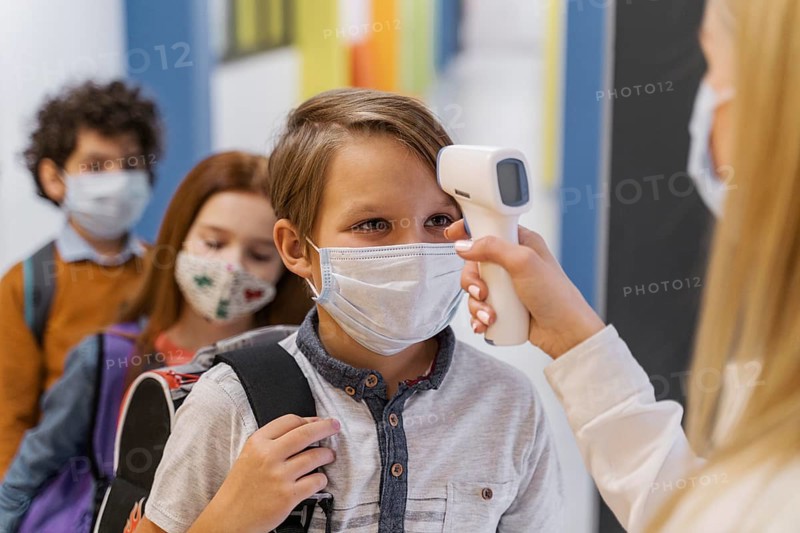 Female teacher with medical mask checking student s temperature school