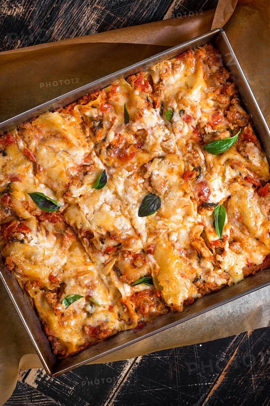 Close-up of a traditional italian lasagna made with minced beef bolognese sauce topped with basil leafs served on a rustic dark wooden table