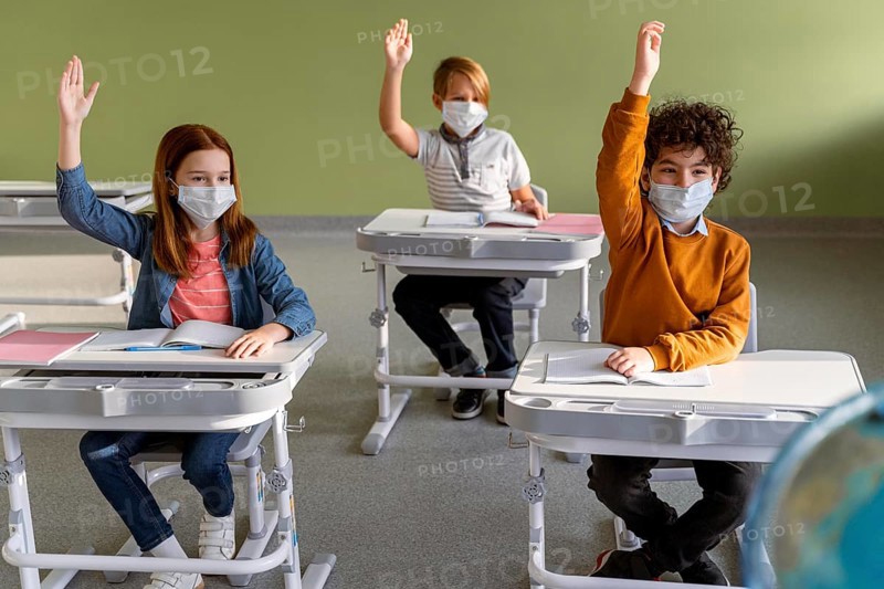 Front view children with medical masks school raising their hands