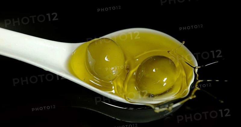 Green Olive, Olea europaea, Falling in a Spoon against Black Background