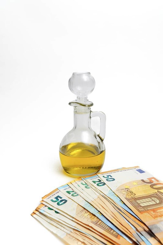 Euro banknotes in front of a bottle of olive oil isolated on a white background, oil price rise concept
