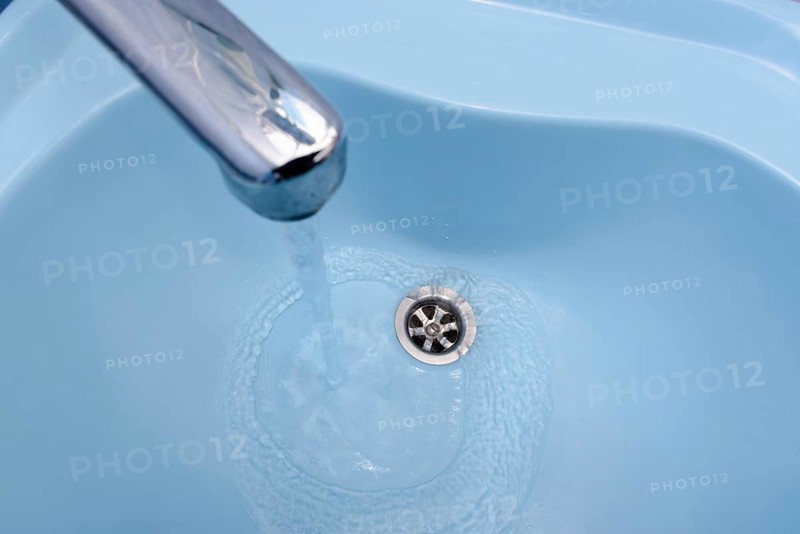 Water flows from the tap in a blue washbasin. The liquid pours out, swirling, in the open plug