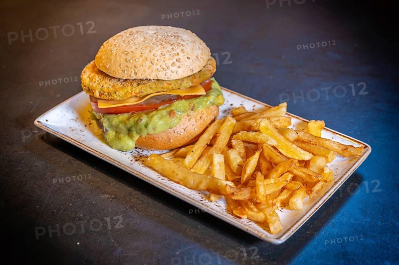 Vegan burger with guacamole and fries on a white plate on a black background