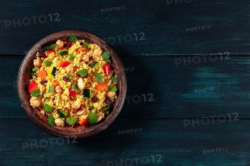Vegan couscous with vegetables, almonds, chickpeas and herbs, shot from above on a dark wooden background with copyspace