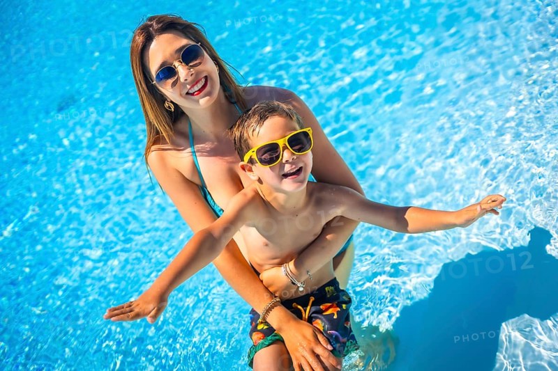 Happy family of a caucasian mother and boy having fun together inside a swimming pool in summer