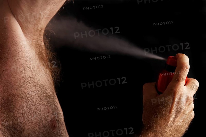 Man with chest hair spraying deodorant into his armpit