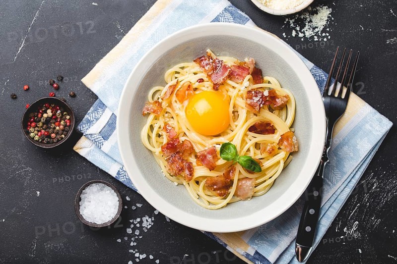 Traditional Italian pasta dish, spaghetti carbonara with yolk, parmesan cheese, bacon in plate on black rustic stone background, top view. Italian dinner with pasta