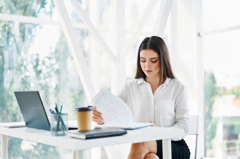 Pretty businesswoman sitting at workplace and reading documents in her modern office. Woman in business, success concept