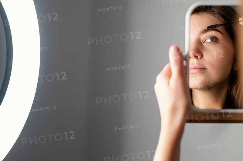 Woman brushing her eyebrows while looking mirror after treatment with copy space