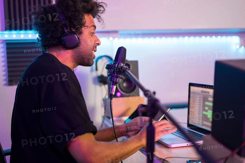 Side view of a musician recording a podcast using microphone and laptop