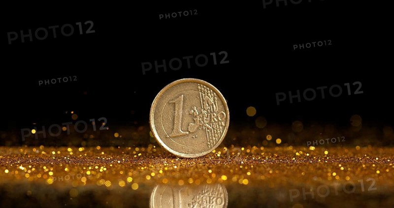 Coin of 1 Euro Rolling on Gold Powder against Black Background