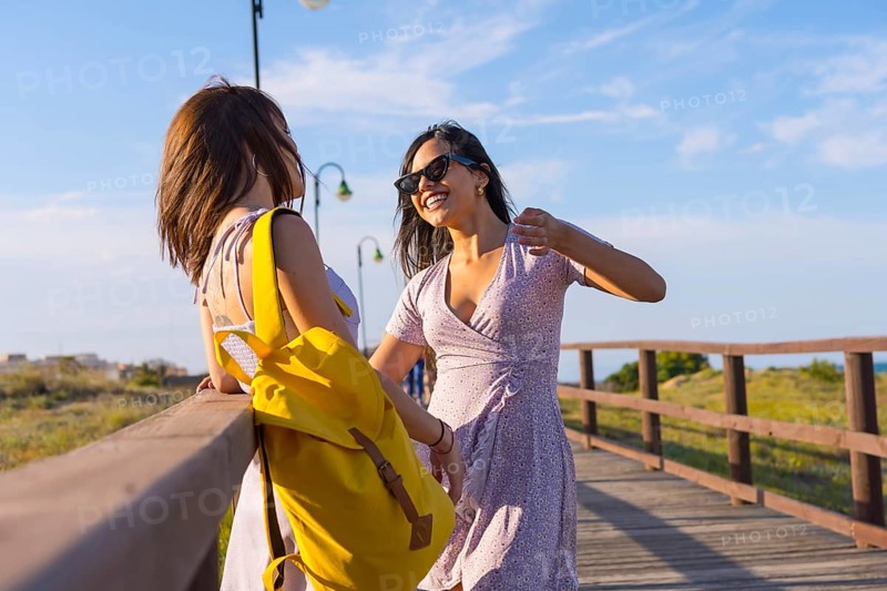 Female friends on summer vacation at the beach talking on a wooden path