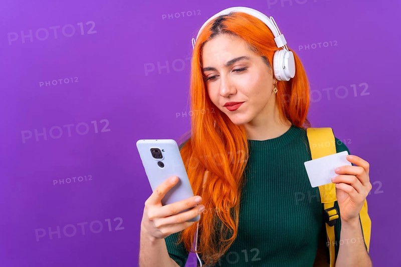 Redhead woman in studio photography online payment with mobile on a purple background