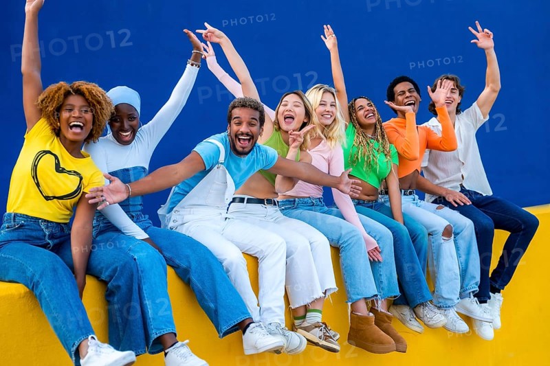 Happy multi-ethnic friends raising hands and smiling sitting in an outdoor wall