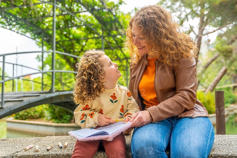 Cute blonde girl reading a book with her mother in the park
