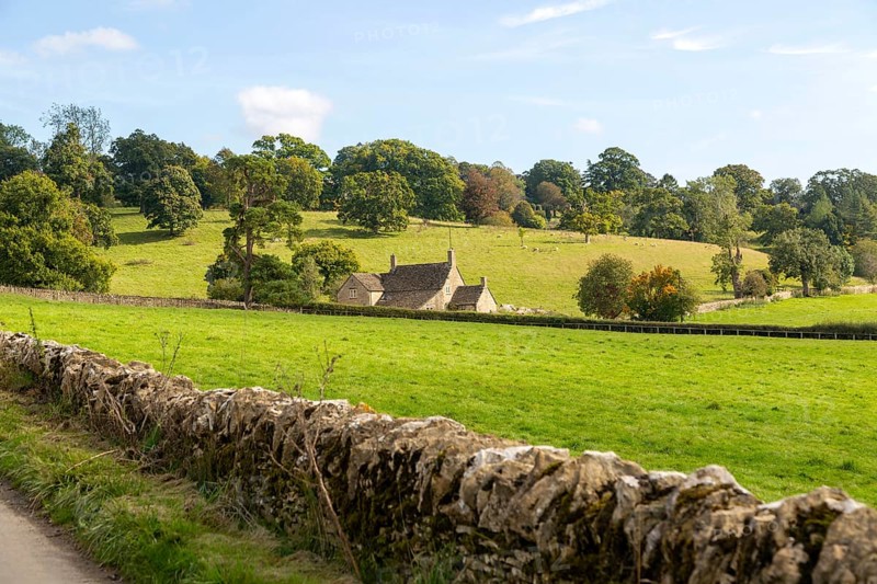 Cotswolds landscape of fields, trees, farmhouse building, near Yanworth, Gloucestershire, England, UK dry stone wall foreground