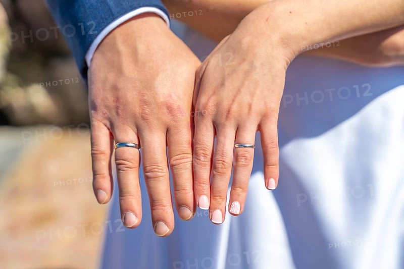 A couple is holding hands and wearing wedding rings. The man's ring is on the left hand and the woman's ring is on the right hand