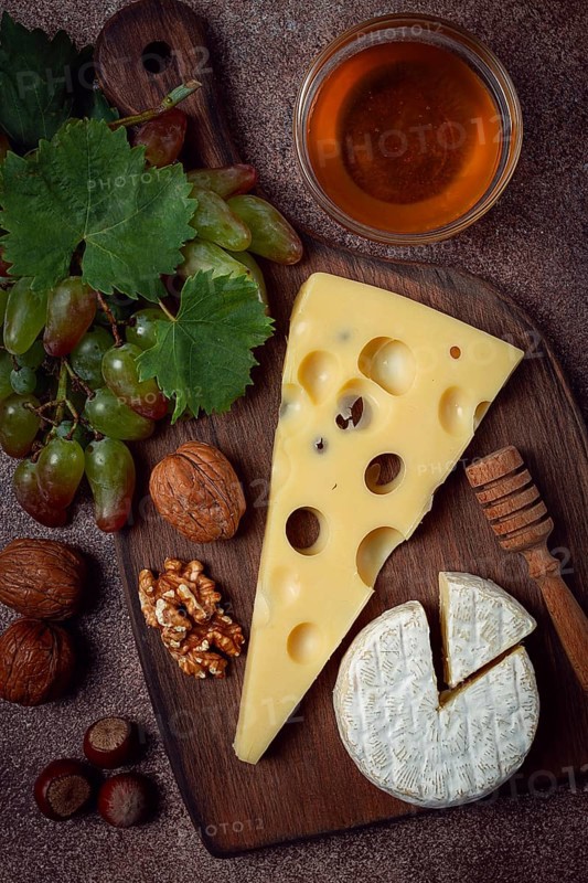 Cheese with big holes, emmental, maasdam, brie cheese, on a cutting board, with grapes and honey, nuts, appetizer to wine, top view