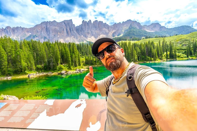 Tourist enjoying the breathtaking view of lake carezza and the dolomites making selfie and thumbs up