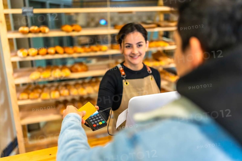 View over shoulder of a young man paying using credit card in a bakery shop