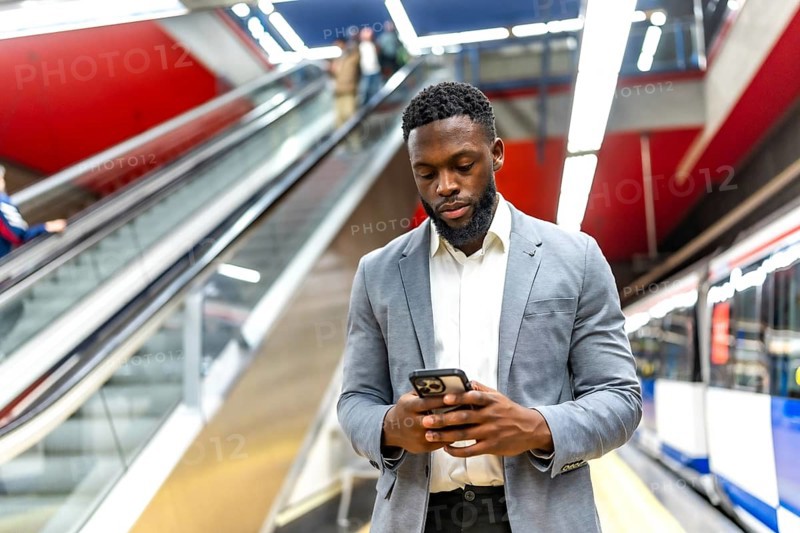 Young businessman waiting for a subway train in a station, using his smartphone to check messages and stay connected while commuting