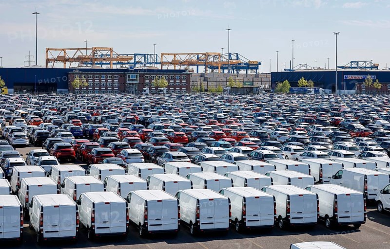 Duisburg, North Rhine-Westphalia, Germany - New cars and vans, car terminal in Duisburg harbour, cranes in the container harbour behind