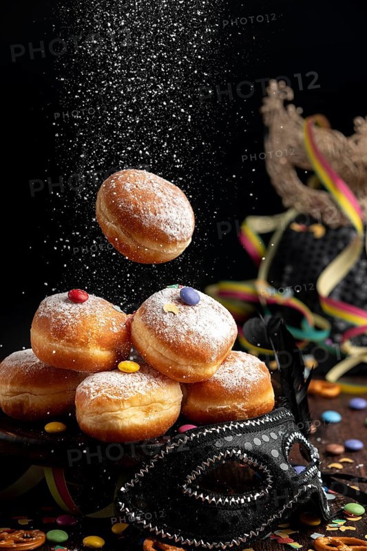 Doughnuts are sprinkled with icing sugar, surrounded by a mask and colourful decorations, carnival