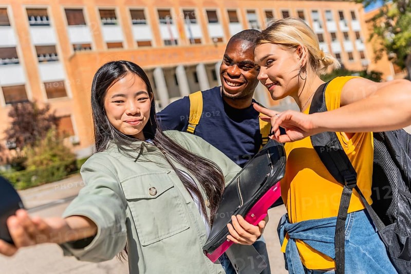 Multi-ethnic university students gesturing success with fingers while taking selfie at the campus