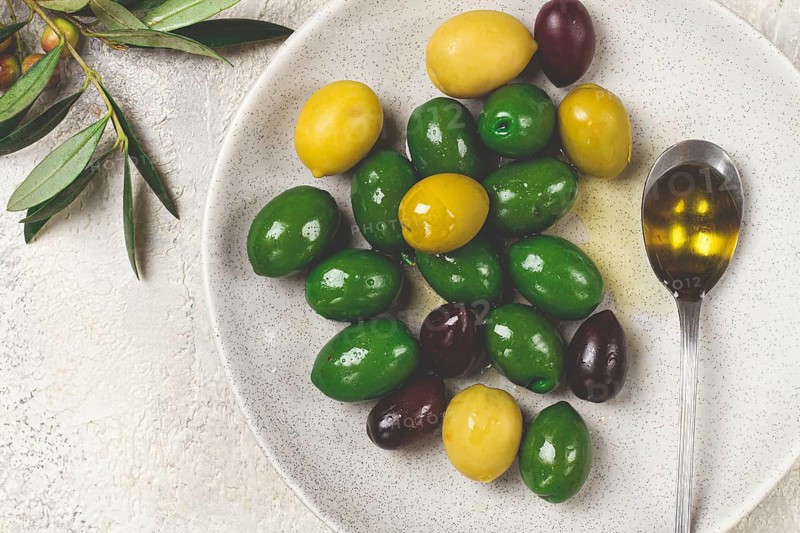 A mix of olives, a variety of Chalkidiki, verdi giganti and Kalamata, on a plate with a spoonful of olive oil, top view, no people