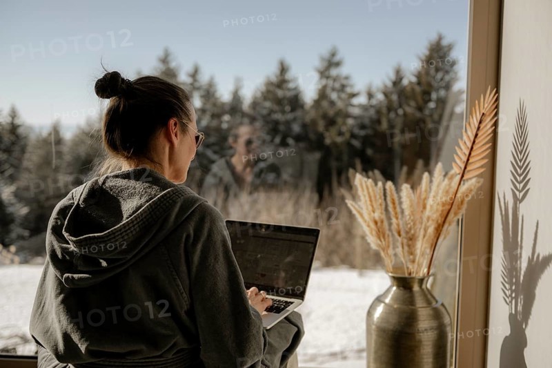 Woman in bathrobe sitting with a laptop on her lap in a garden