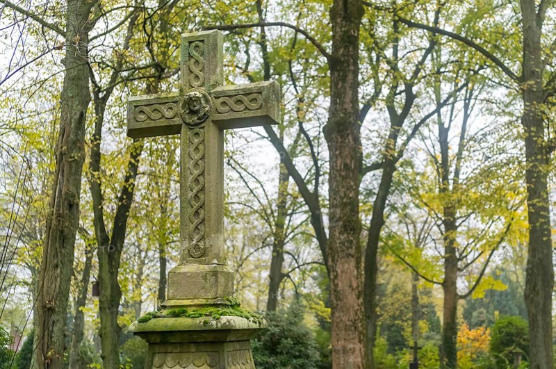 Old weathered celtic cross tombstone standing in a peaceful cemetery during fall