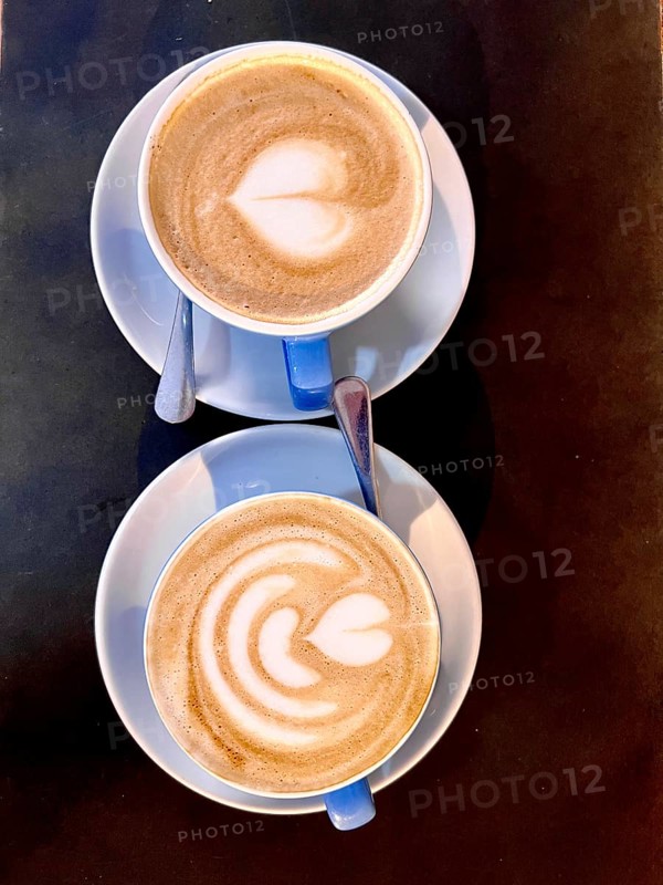 Top-down view of two cappuccinos with heart-shaped latte art, served in blue cups on a dark table.