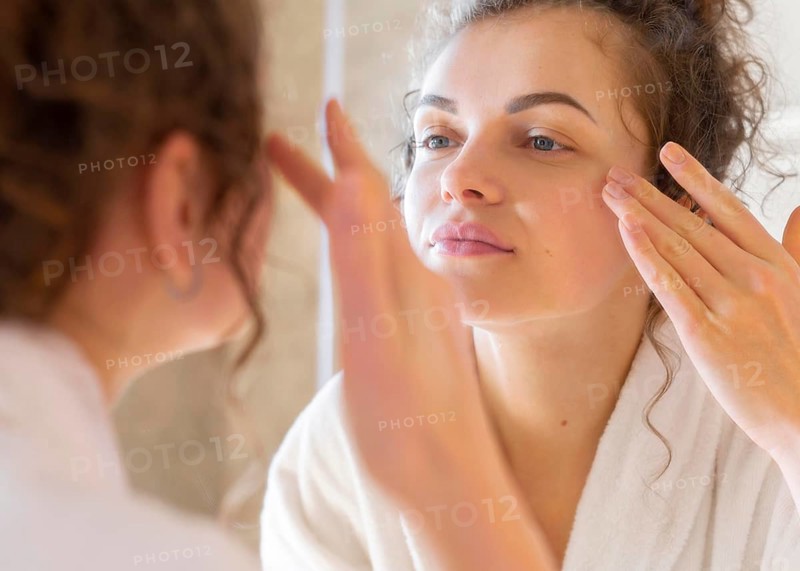 Woman applying cream face while looking mirror 2
