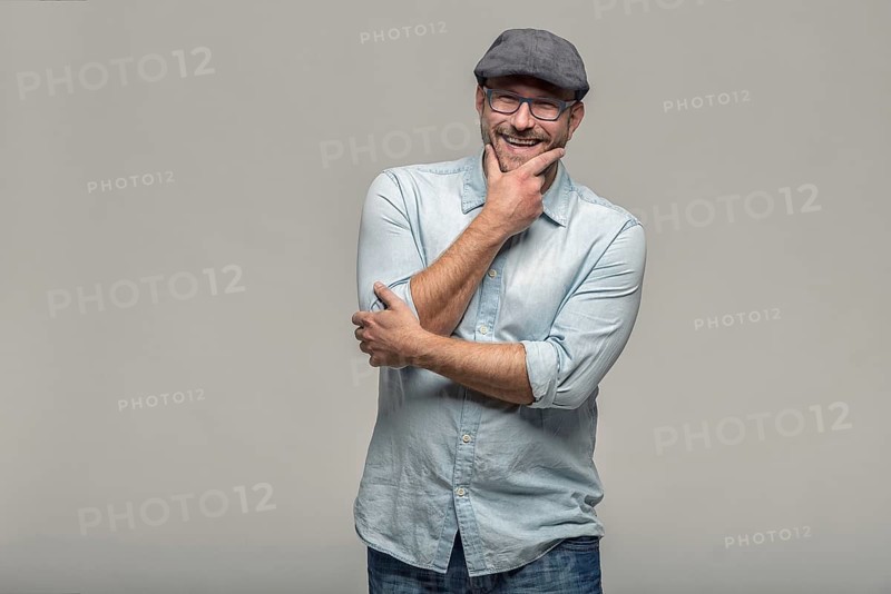 Thoughtful attractive middle-aged man with his finger to his mouth standing looking towards the camera on a grey background