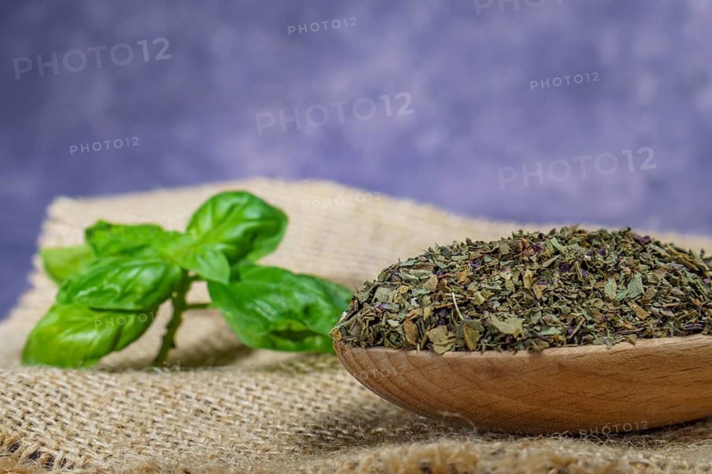 Dried basil ground in a wooden spoon with freshly cut basil leaves on a burlap cloth