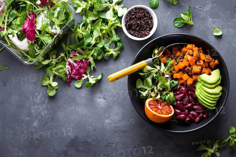 Quinoa salad in bowl with avocado, sweet potato, beans, herbs, orange on concrete rustic background. Quinoa superfood concept. Clean healthy detox eating. Veganvegetarian food. Making healthy salad