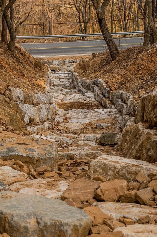 Drainage ditch constructed of large boulders on side of mountain on early spring afternoon in South Korea