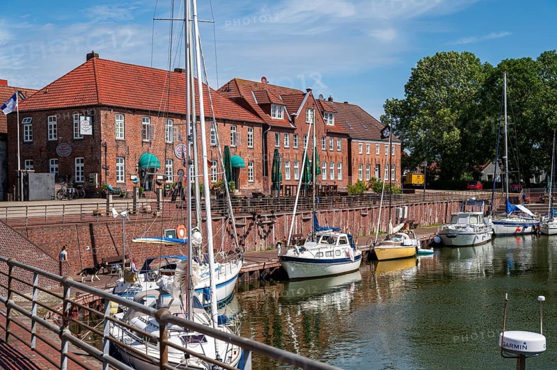 Sailing yachts on the promenade with brick houses and a terrace in sunny weather and blue sky, Hooksiel, Wangerland, Lower Saxony