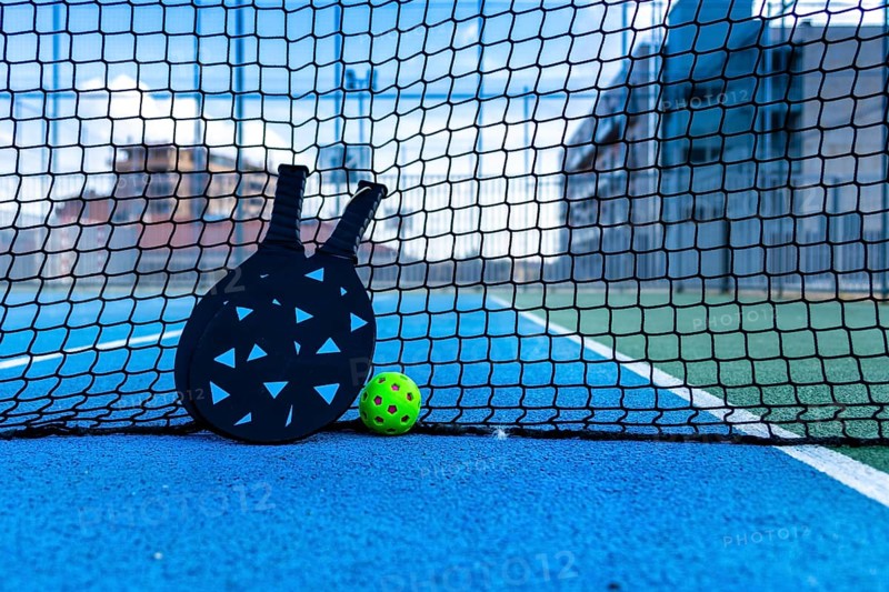Pickleball ball and paddles resting on the net of a pickleball court