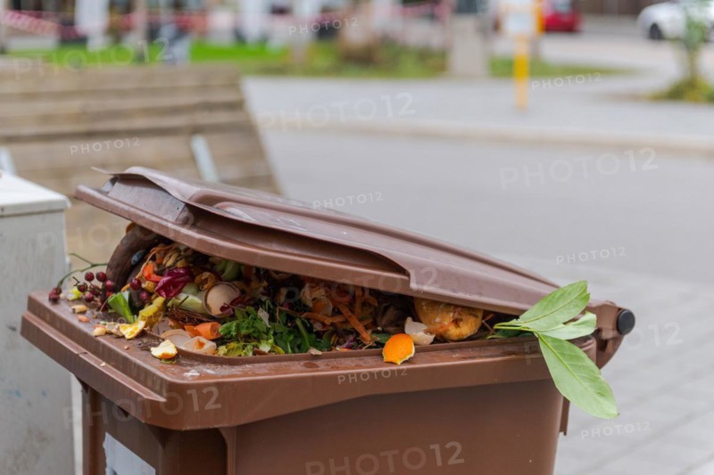 Brimful municipal bio-waste trash can with open lid for biological organic waste standing on open street in residential area after christmas holidaysv
