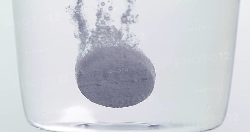 Tablets Falling and Dissolving into a Glass of Water against White Background