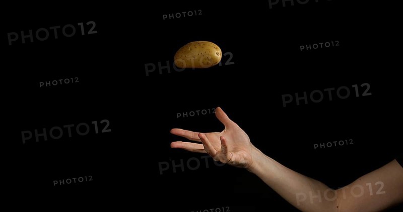 Hand of Woman Throwing a Potatoe against Black Background