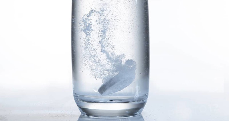 Tablets Falling and Dissolving into a Glass of Water against White Background