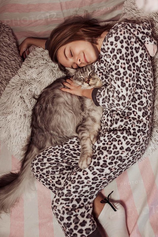 Girl pajamas hugging her cat laying bed