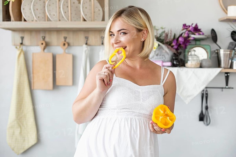 Beautiful pregnant woman eating yellow pepper