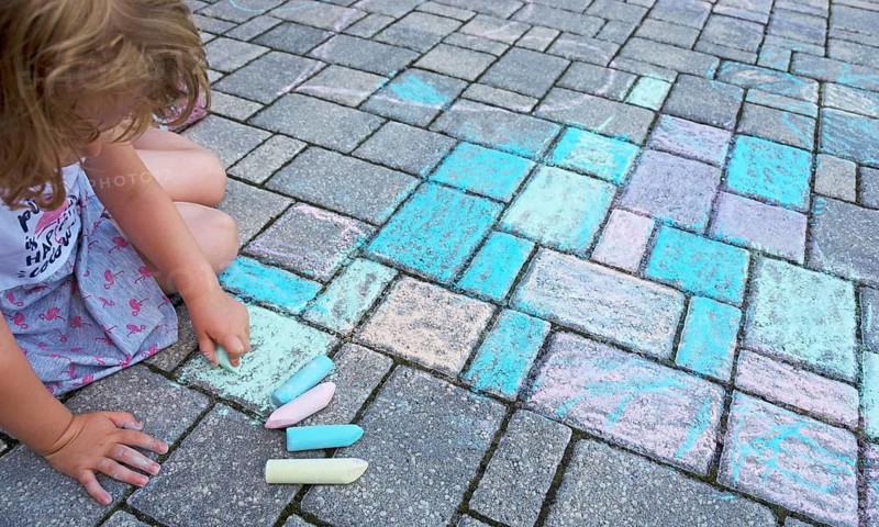 Child paints with colorful chalk on concrete pavement