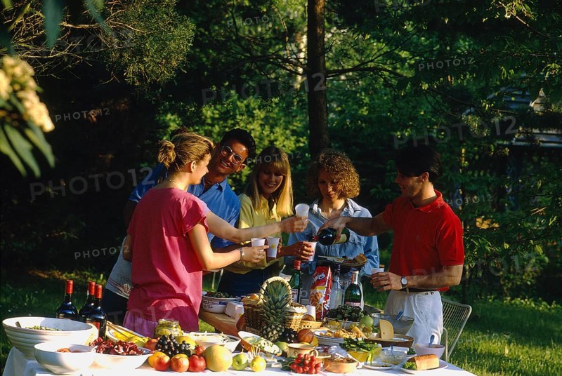 Garden party, food and drink, richly laid table, fruit, vegetables, fruits, bread, cheese, wine plates, bowls, young people, 3 woman, 2 men, 5 people, toast, picnic, eating outdoors