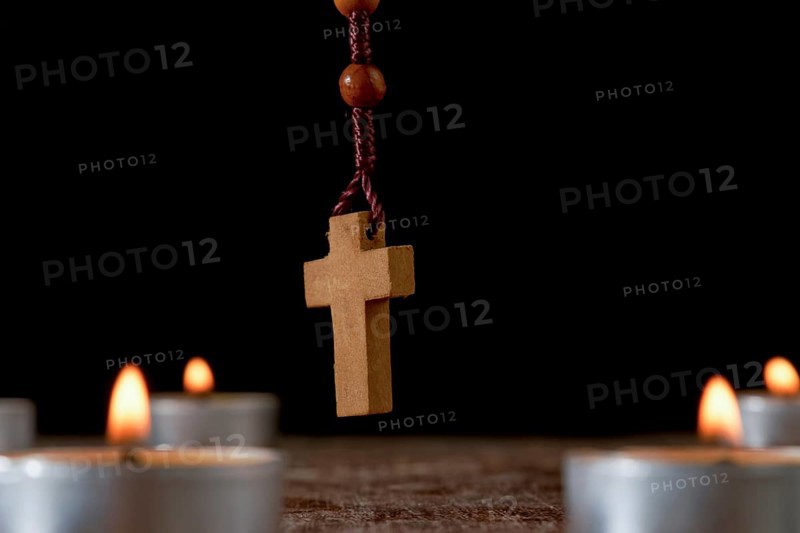 Circle of lighted candles with a wooden Rosary praying beads in the center and a smoldering incense in the background isolated on a black background