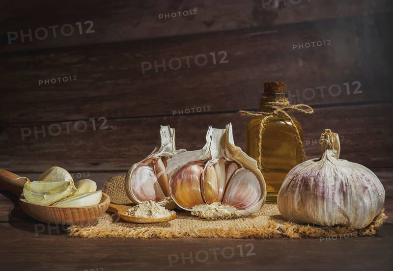 Whole, powdered and chopped garlic on a burlap cloth with a glass bottle with olive oil on a wooden table